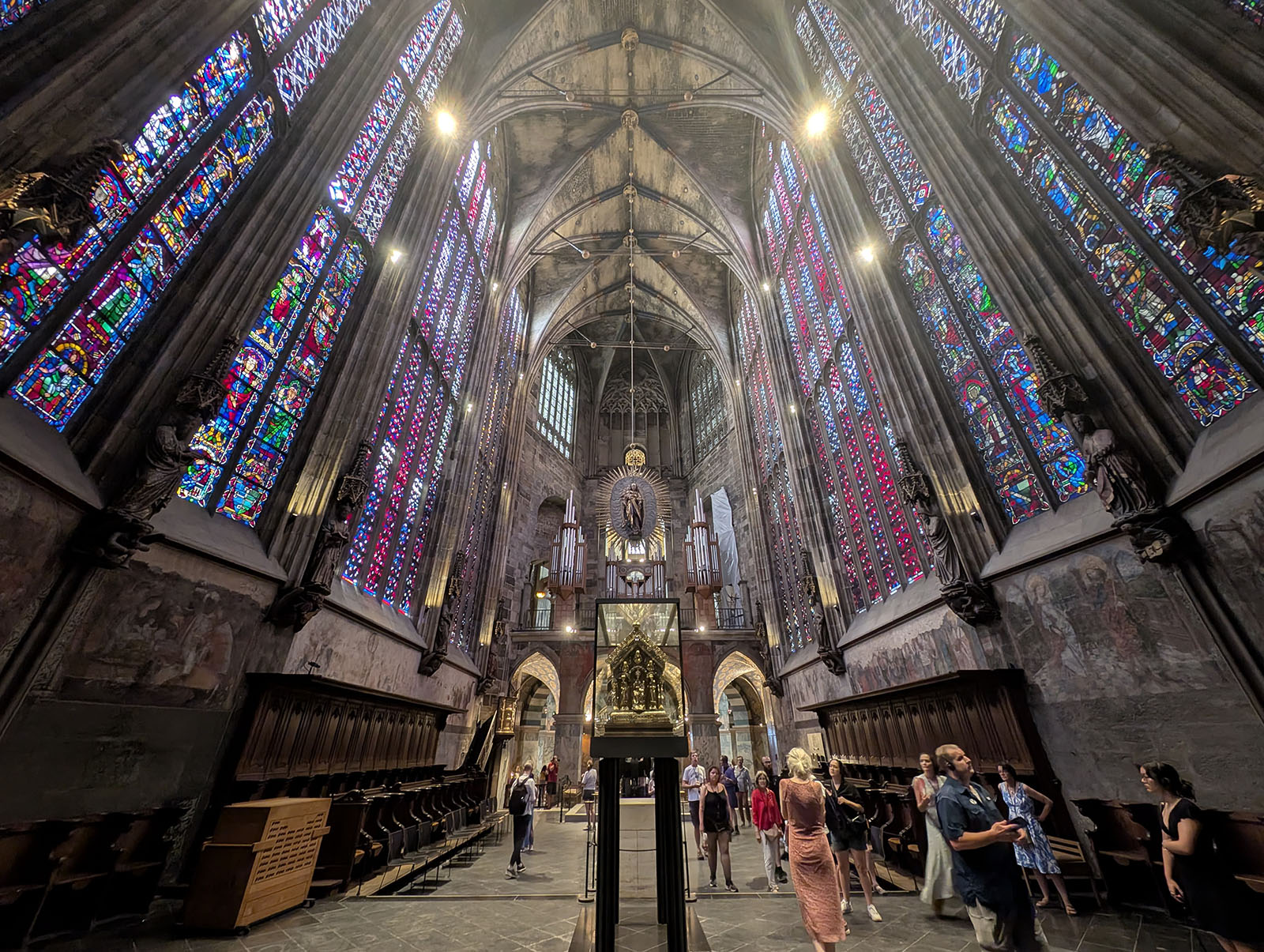 Tall choir in a gothic style. Stained glass either side, golden reliquaries on stands in the centre.